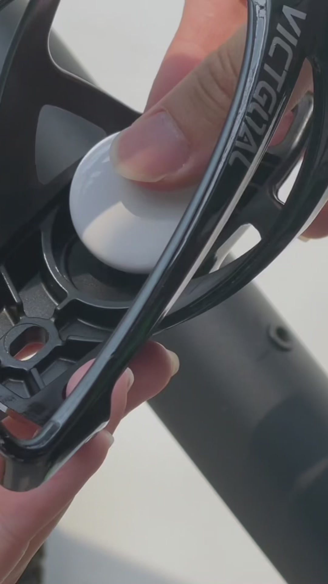 Close-up of an AirTag being fitted into the bike bottle cage mount