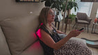 Woman using a red light wrap on her neck and shoulder while seated